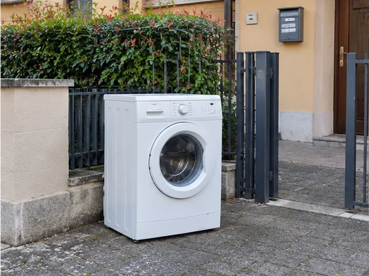 Lavatrice bianca lasciata da sola all’esterno vicino a un cancello residenziale
