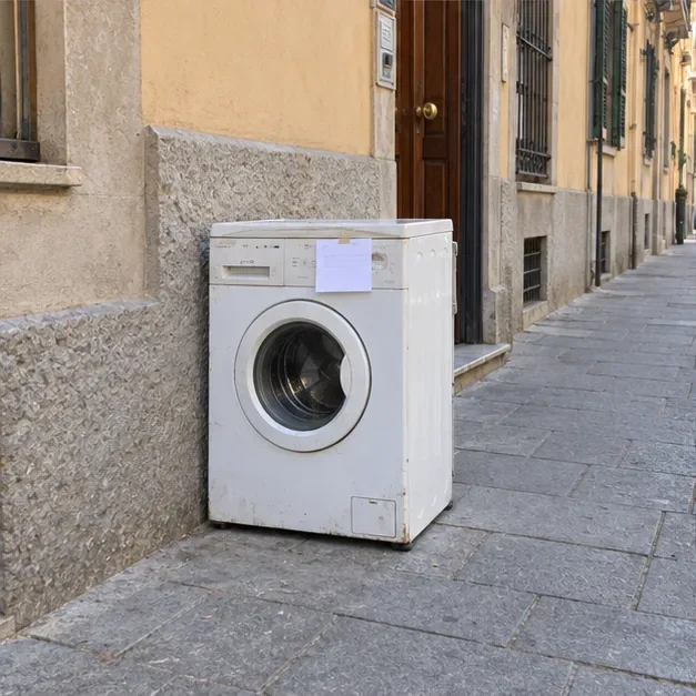 Una lavatrice lasciata sul marciapiede accanto alla facciata per il ritiro prenotato, con un cartello applicato sul davanti.