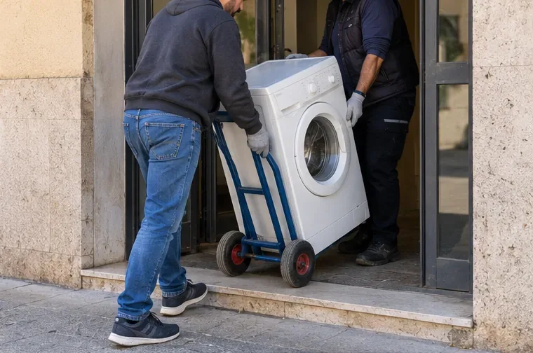 Due persone spostano una lavatrice con un carrello attraverso l'ingresso di un edificio