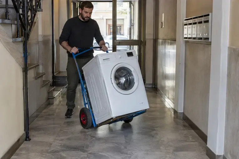 Persona che sposta una lavatrice su un carrello manuale in un corridoio condominiale
