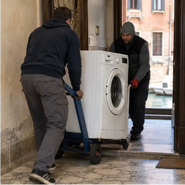 Due persone spostano una lavatrice su un carrello attraverso l’ingresso di un edificio veneziano