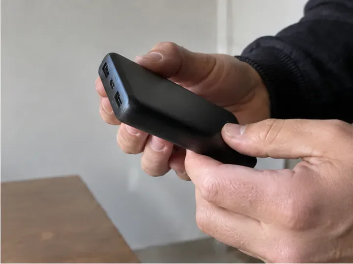 Mani che controllano l’involucro di una power bank nera per verificare rigonfiamenti o danni