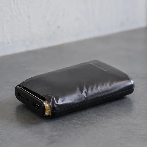 Una power bank nera visibilmente gonfia e deformata appoggiata su una superficie dura non combustibile