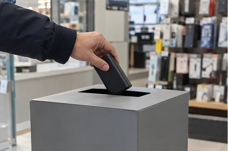 Una mano consegna una power bank integra verso un contenitore dedicato alla raccolta delle batterie