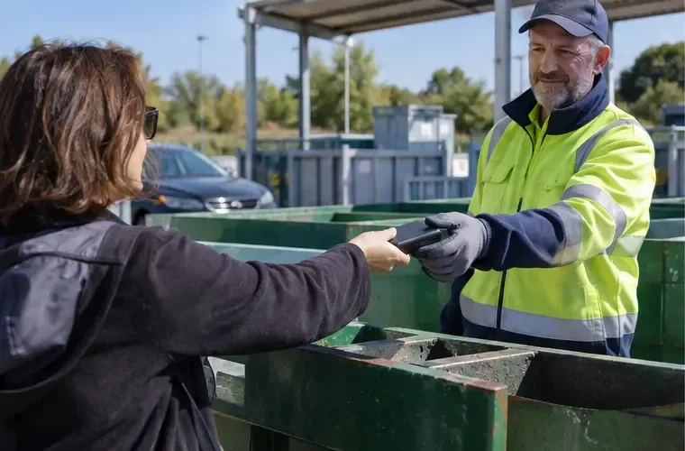 Una cittadina consegna una power bank a un operatore con abbigliamento ad alta visibilità presso un centro di raccolta