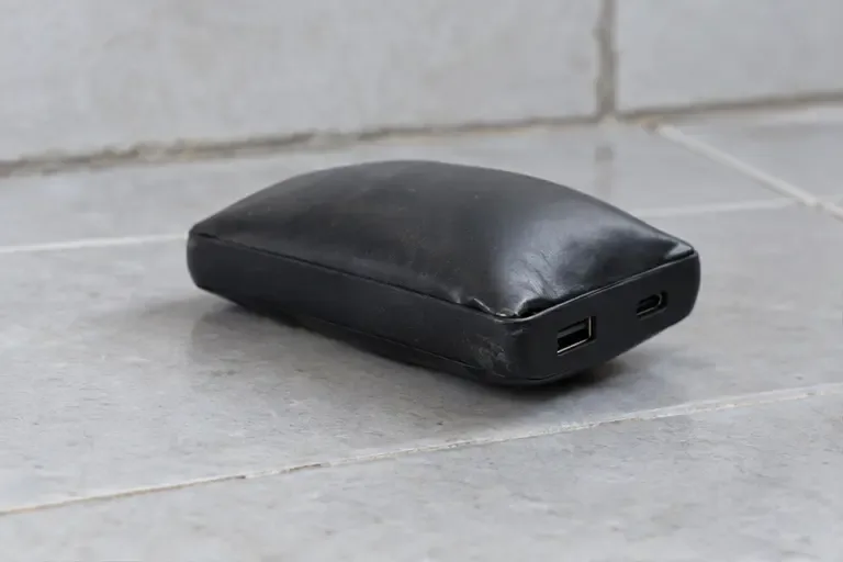 Power bank nera visibilmente gonfia appoggiata su piastrelle fredde, scollegata e lontana da materiali infiammabili