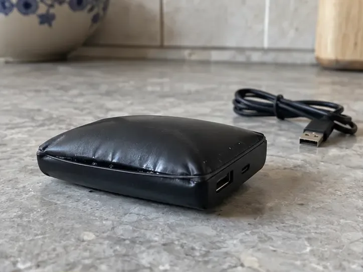 Power bank nera visibilmente gonfia su una superficie in ceramica, con il cavo di ricarica scollegato e distante