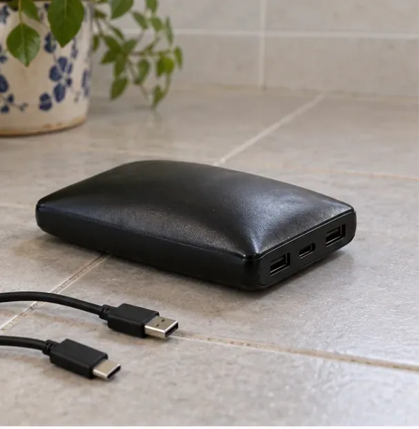 Power bank nera con la custodia chiaramente bombata, scollegata e appoggiata su una superficie piastrellata