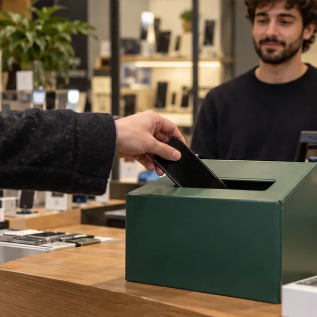 Una persona deposita uno smartphone usato in un contenitore per piccoli apparecchi elettronici in un negozio