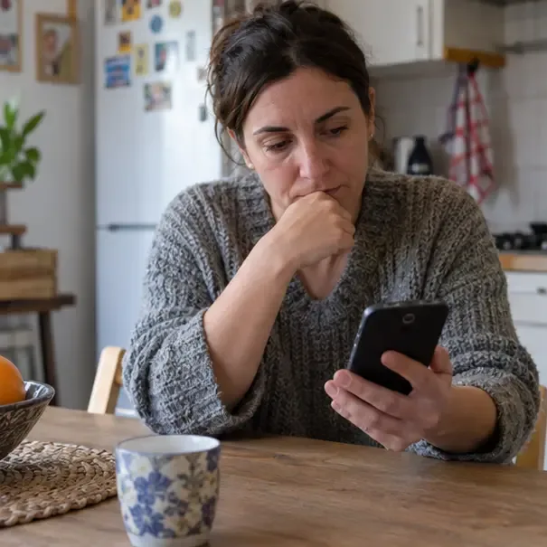 Una persona osserva un vecchio smartphone al tavolo di casa per valutarne il riuso o il riciclo