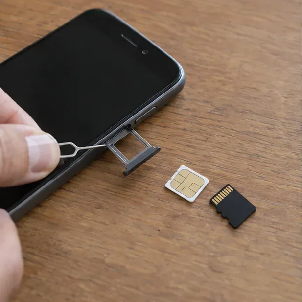 Una mano estrae il carrellino SIM da uno smartphone spento, con SIM e scheda microSD appoggiate sul tavolo