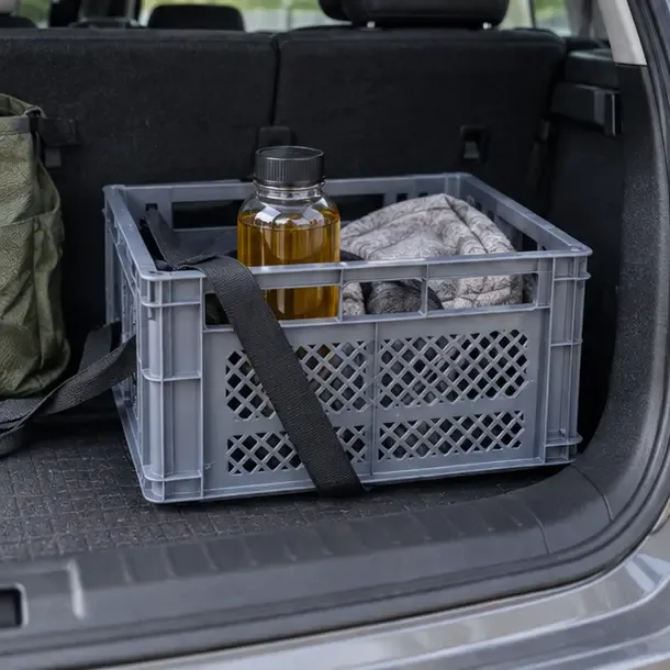 Récipient fermé contenant de l’huile usagée placé verticalement dans une caisse stable dans le coffre d’une voiture