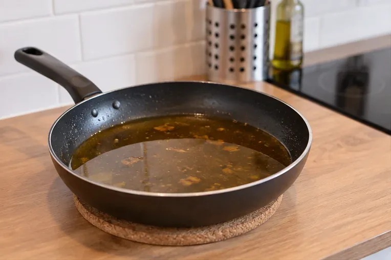 Poêle contenant de l’huile de cuisson usagée refroidissant sur un dessous-de-plat dans une cuisine