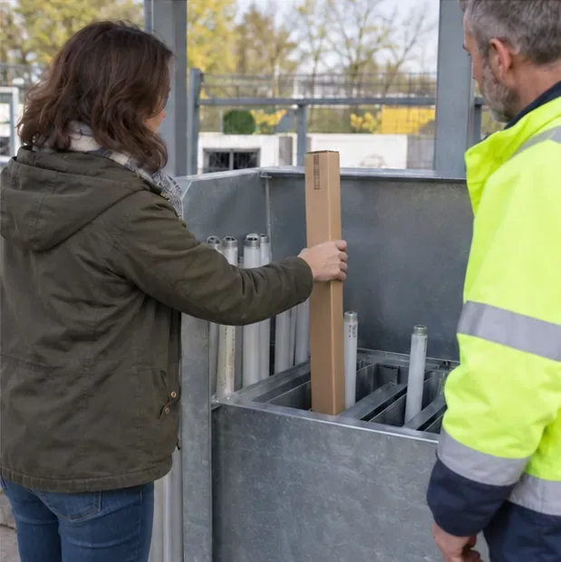 Une personne remet un tube fluorescent protégé dans un grand contenant de collecte dédié, sous l’indication d’un agent