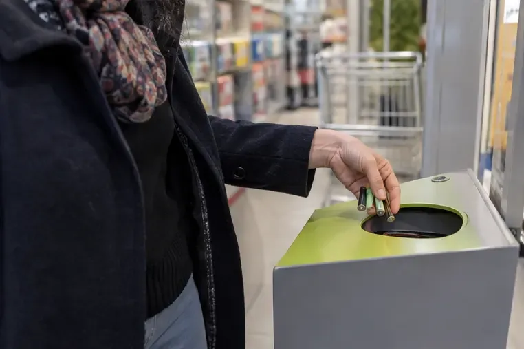 Une personne dépose plusieurs piles ordinaires dans une borne de collecte dédiée située à l’intérieur d’un magasin