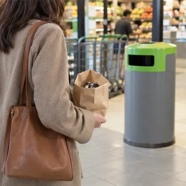 Une personne transporte un sac en papier contenant des piles usagées vers une borne de collecte dans un magasin