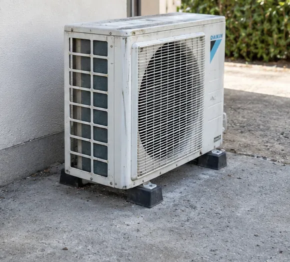 Une unité extérieure blanche repose sur ses supports au sol, avec sa grille et son carter en place.