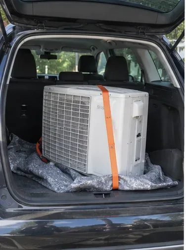 Une unité de climatiseur est maintenue verticalement dans le coffre d’une voiture avec une sangle.