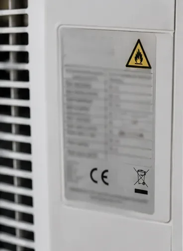 Gros plan sur la plaque signalétique d’un climatiseur avec les symboles réglementaires visibles.