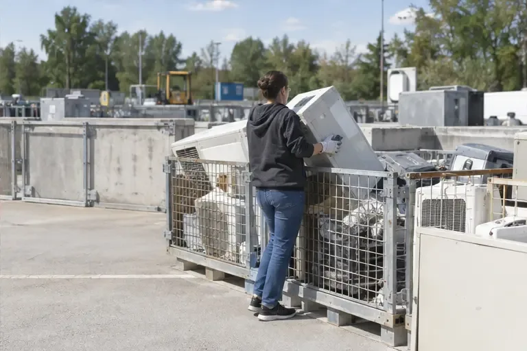 Une personne dépose un appareil électrique dans une zone grillagée d’un centre de recyclage