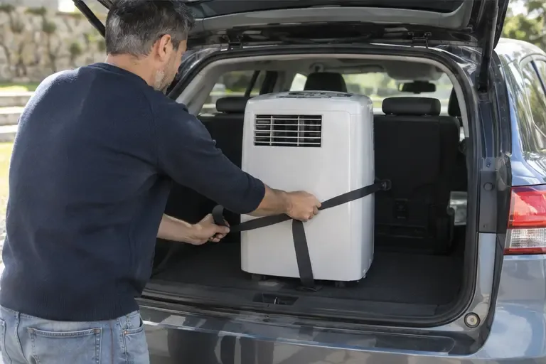 Un climatiseur mobile est maintenu debout et attaché par une sangle dans le coffre d’une voiture