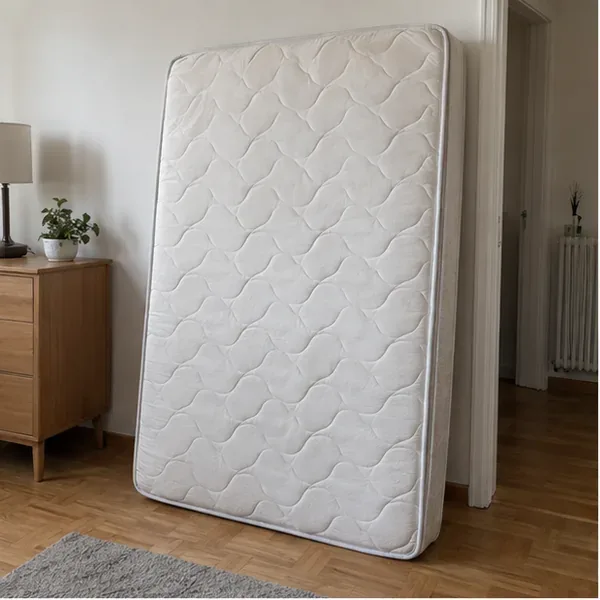 Un matelas propre est posé verticalement dans une pièce, prêt à être évacué