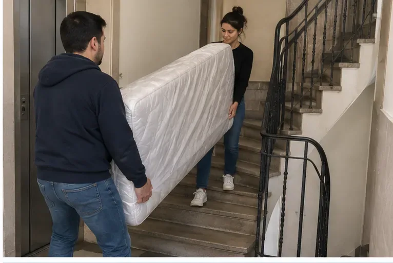 Deux personnes portent un matelas verticalement dans la cage d’escalier d’un immeuble