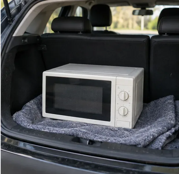 Micro-ondes posé à plat dans le coffre d’une voiture sur une couverture pour éviter les chocs pendant le trajet