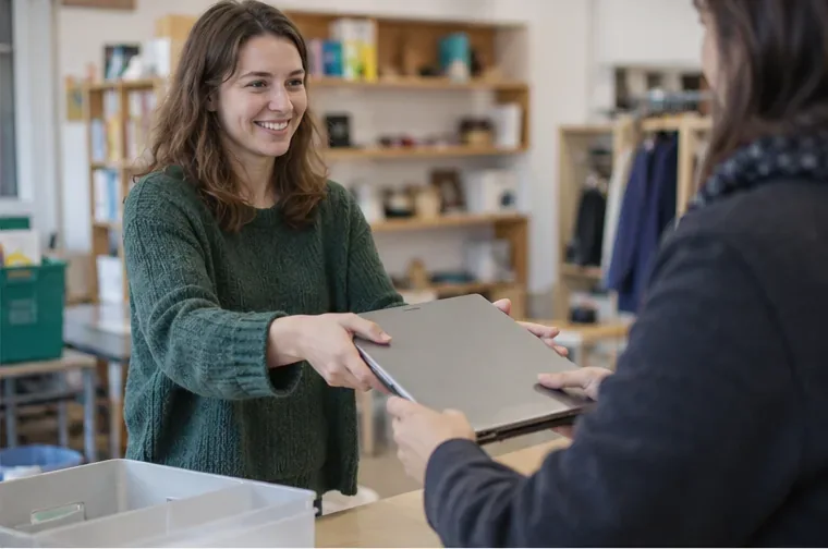 Une personne remet un ordinateur portable à une autre personne dans un espace de réemploi, après préparation de l’appareil.