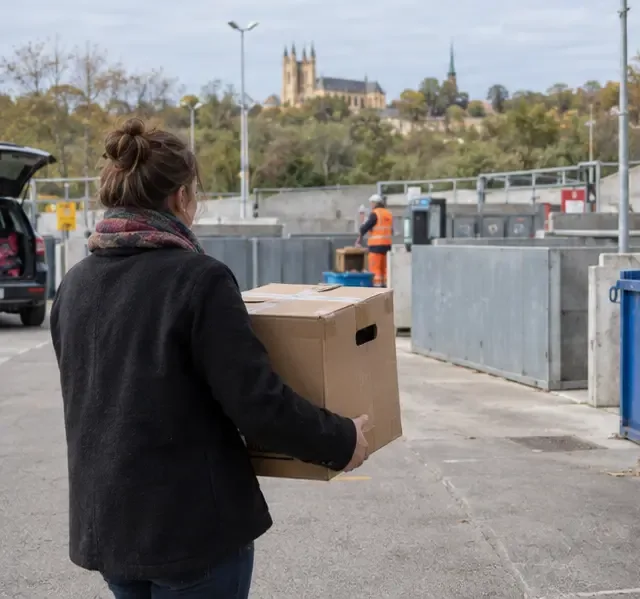 Une habitante transporte un carton contenant un ancien ordinateur vers une zone de dépôt municipale