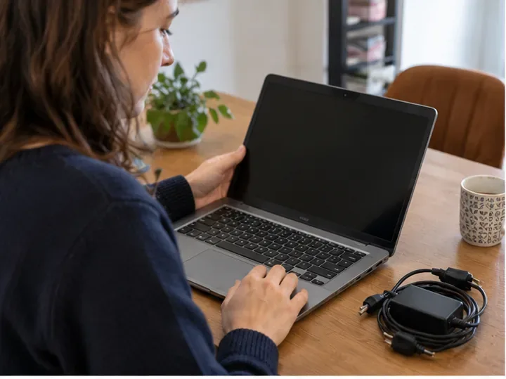 Une personne examine un ordinateur portable ancien posé sur une table, avec son chargeur à côté.