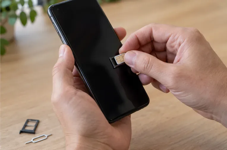 Des mains retirent la carte SIM d’un smartphone posé au-dessus d’une table en bois.