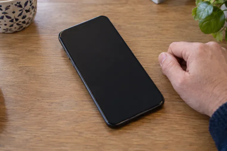 Smartphone intact à écran noir posé sur une table à côté d’une main