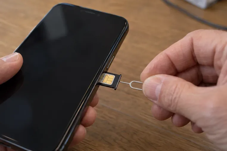 Main tenant un smartphone avec son tiroir SIM ouvert et un petit outil d’éjection près de la carte