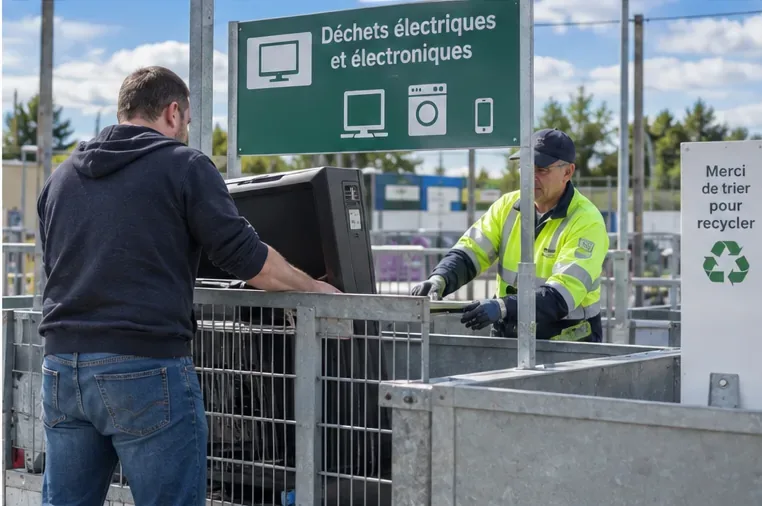 Un particulier remet un téléviseur dans une zone dédiée aux déchets électriques et électroniques avec l’aide d’un agent