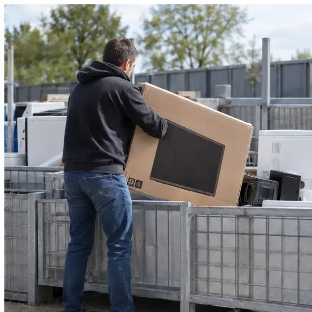 Une personne dépose un téléviseur emballé dans une zone organisée de collecte des appareils électriques