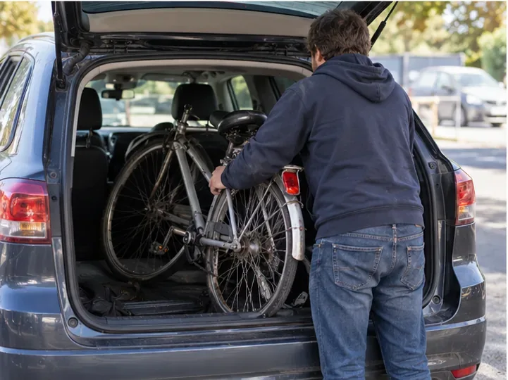 Un homme charge un vélo usagé dans le coffre ouvert d’une voiture avant de partir vers un point de collecte.