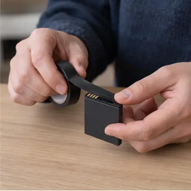Des mains posent un ruban isolant sur les bornes d’une petite batterie lithium-ion intacte