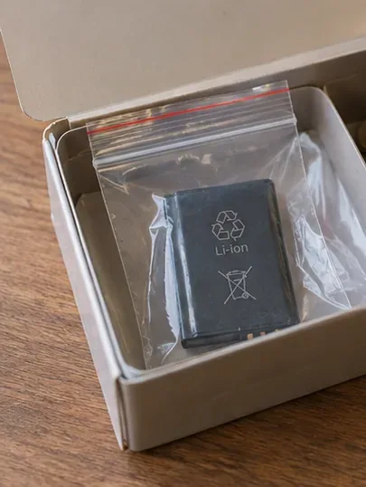 Petite batterie lithium-ion placée seule dans un sachet transparent à l’intérieur d’une petite boîte en carton.