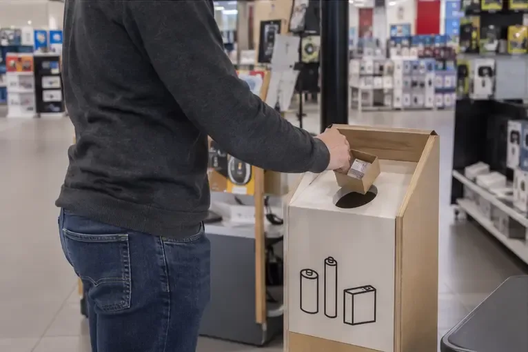 Une personne dépose une petite batterie dans un conteneur de collecte situé dans un magasin d’électronique