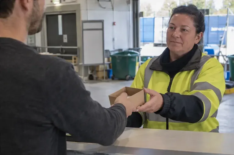Un agent en gilet haute visibilité reçoit une boîte contenant une batterie dans un centre de recyclage