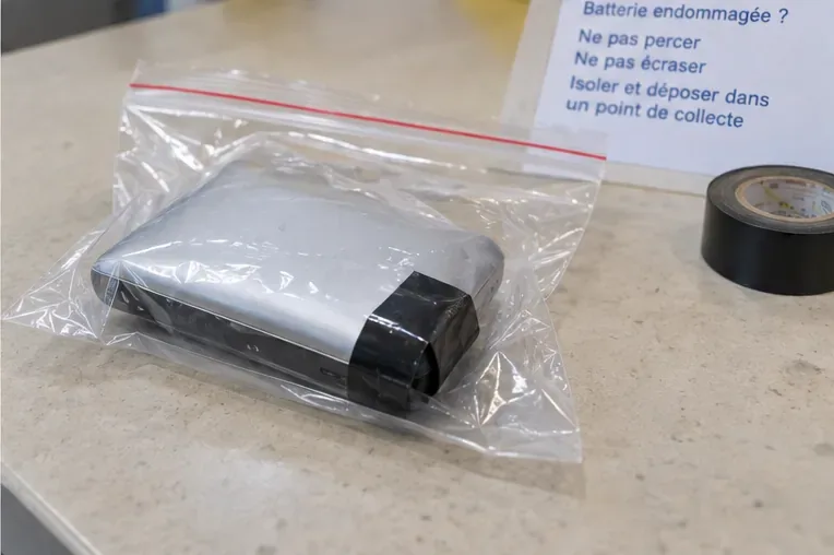 Une batterie externe visiblement gonflée est isolée dans un sac plastique transparent fermé, avec ses connectiques protégées.