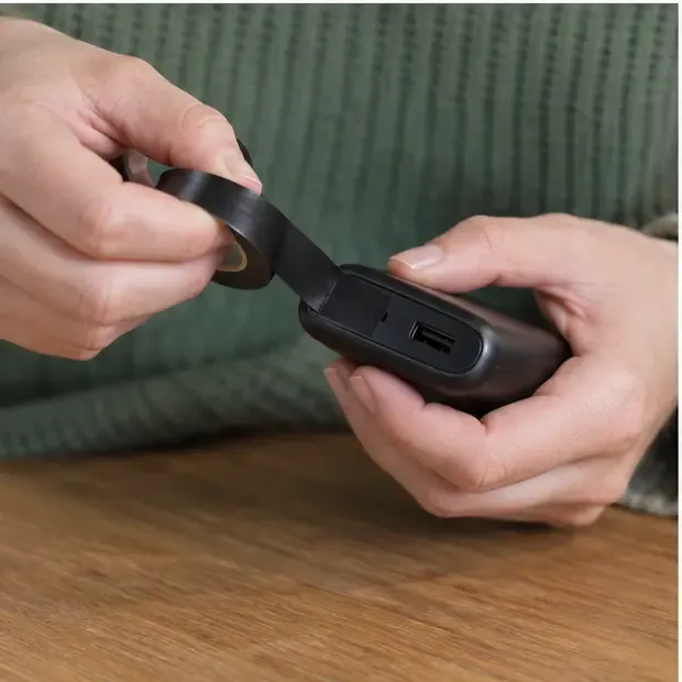 Mains qui posent une bande isolante sur les contacts accessibles d’une batterie externe