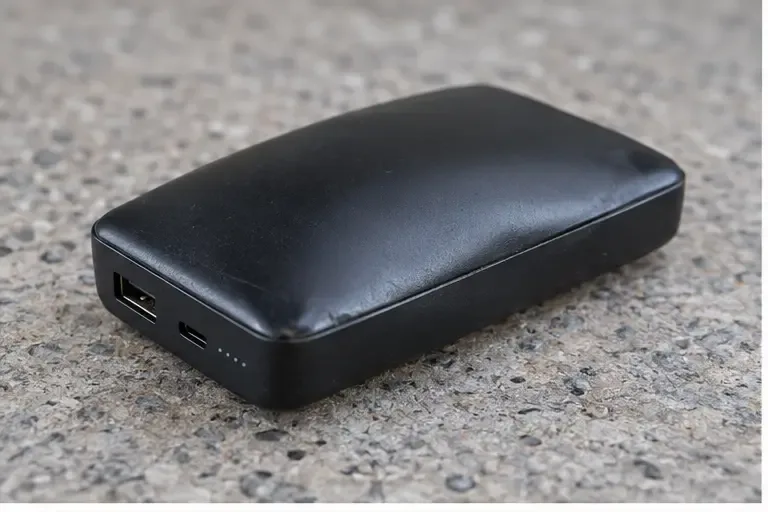 Batterie externe noire dont la coque est légèrement bombée sur une surface minérale