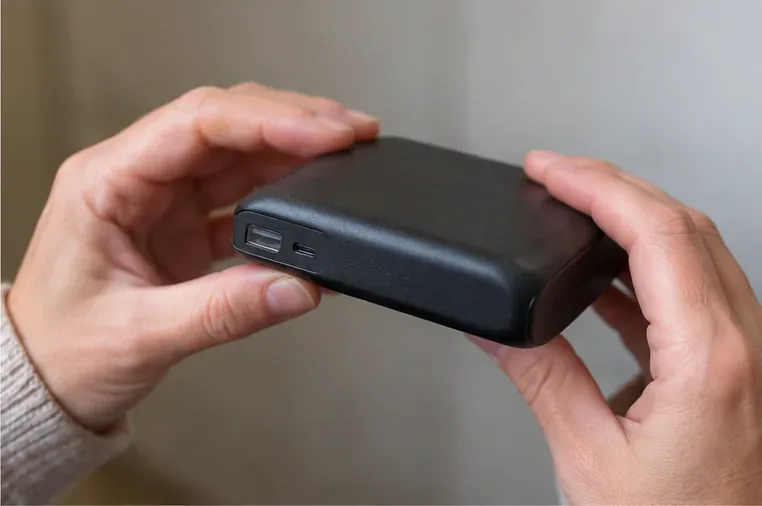 Gros plan de deux mains examinant la coque et les ports USB d’une batterie externe noire