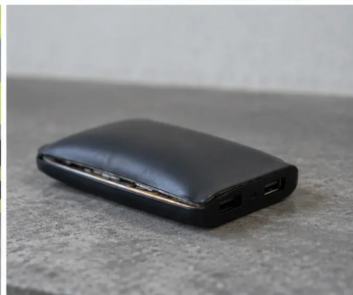 Une batterie externe noire dont le boîtier est gonflé et entrouvert, posée seule sur une surface minérale