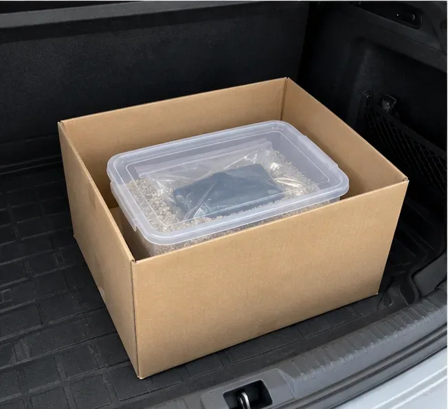 Bac contenant une batterie externe isolée et immobilisée dans un carton stable dans le coffre d’une voiture