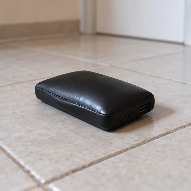 Batterie externe noire dont la coque est bombée, posée seule sur un sol carrelé
