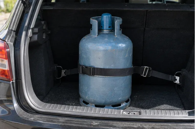 Une bouteille de gaz est maintenue droite et sanglée dans le coffre d'une voiture pour éviter tout déplacement pendant le trajet