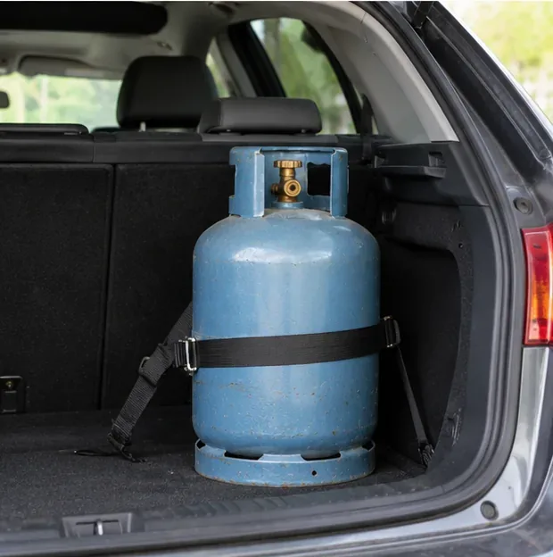 Une bouteille de gaz maintenue verticalement par une sangle dans le coffre ouvert d'une voiture